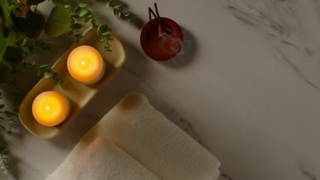 Overhead-View-Looking-Down-On-Still-Life-Of-Lit-Candles-And-Incense-Stick-With-Green-Plant-And-Towels-As-Part-Of-Spa-Day-Decor-1